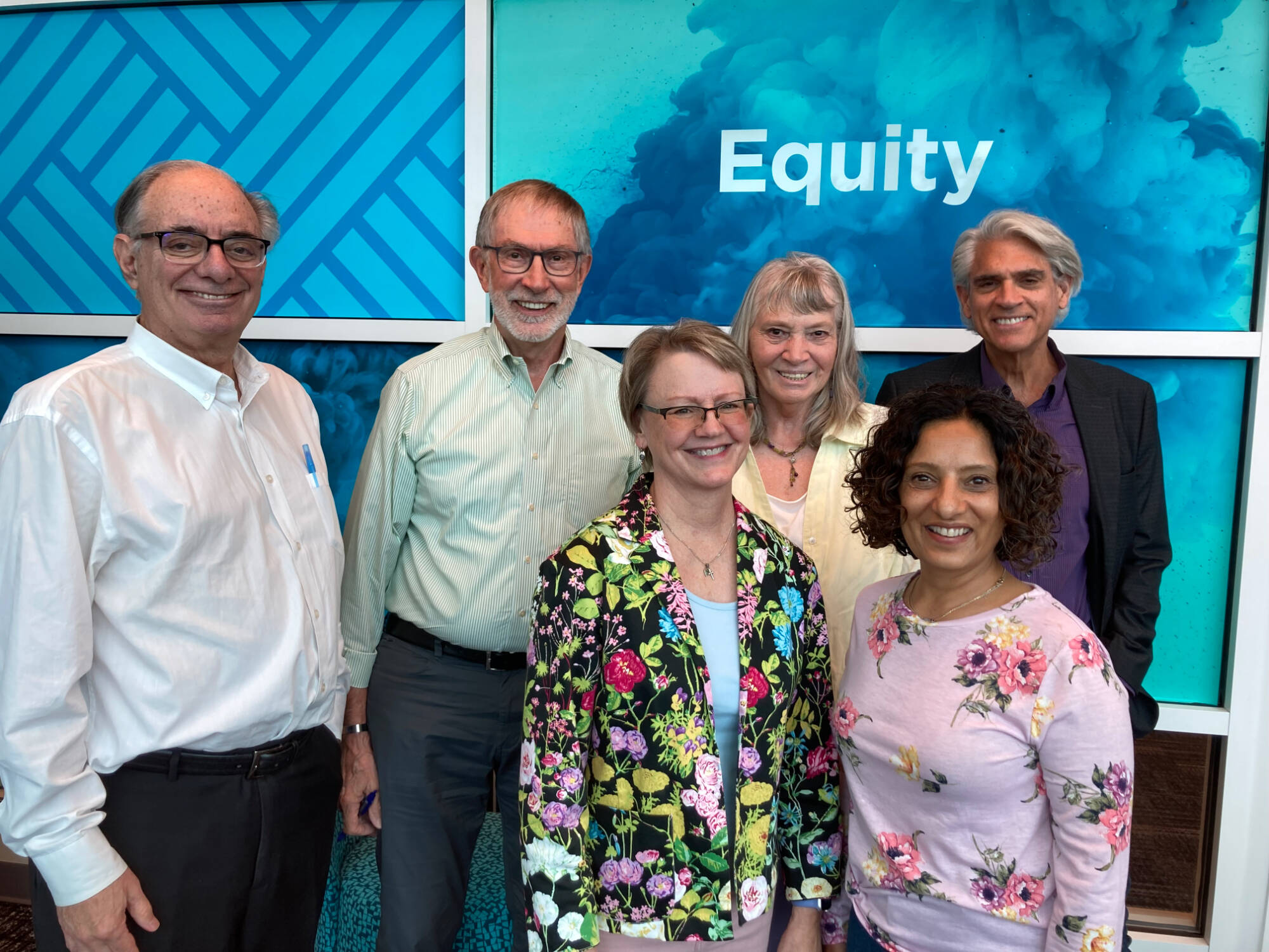 A group of adults posing for a photo in front of a colorful background - the Kaufman Associates.